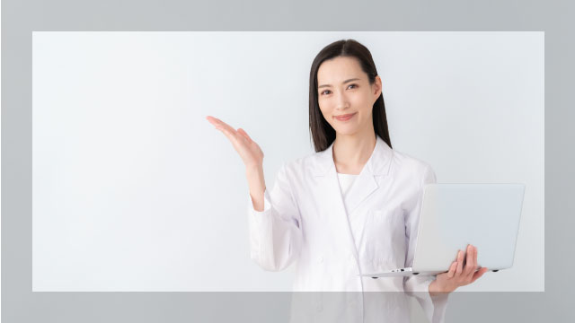 白衣を着た女性が片手でパソコンを持ち、もう一方の手で前方を示している