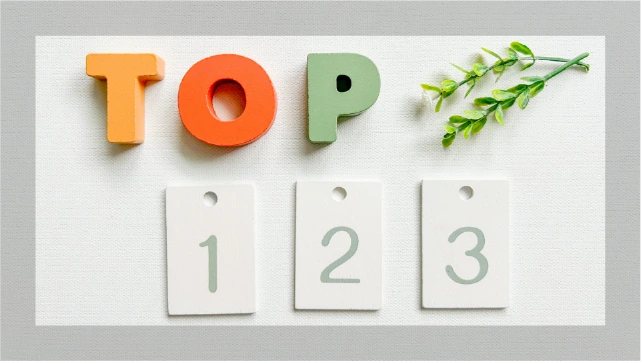 「TOP」と書かれたカラフルな木製文字と、1〜3の数字プレートを並べたフラットレイ。整形施術ランキングのイメージに使用。