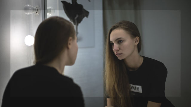 鏡に映る顔を真剣に見つめる若い女性が自分の左右差を確認している様子