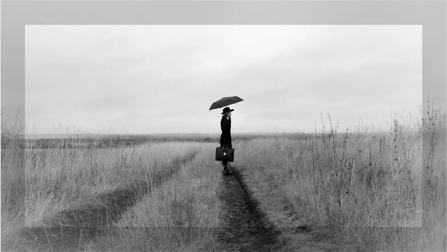 草原の中で傘をさす女性の後ろ姿。コンプレックスを抱える孤独感と静けさを象徴するイメージ。